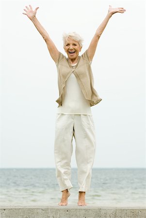 Senior woman standing on tiptoe at the beach, arms raised, smiling Stock Photo - Premium Royalty-Free, Code: 632-02008081