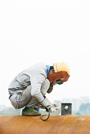 Welder crouching on metal pipe, looking down, side view Stock Photo - Premium Royalty-Free, Code: 632-02038738