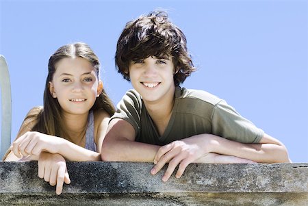 Brother and sister side by side, leaning on concrete wall, smiling at camera, portrait Stock Photo - Premium Royalty-Free, Code: 632-02128261