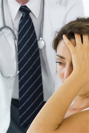 Woman holding head, looking away, doctor in background Stock Photo - Premium Royalty-Free, Code: 632-02227652