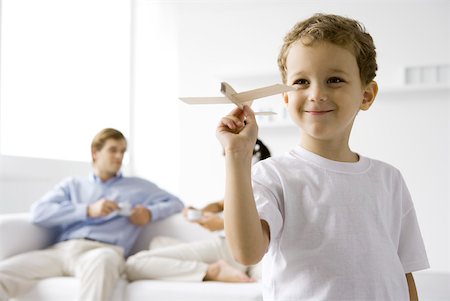 father and son with toy airplane - Boy playing with toy airplane, parents sitting on couch in background Stock Photo - Premium Royalty-Free, Code: 632-02227821