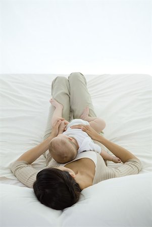 simsearch:632-02689996,k - Woman lying on bed, holding infant on her stomach, rear view Stock Photo - Premium Royalty-Free, Code: 632-02282499