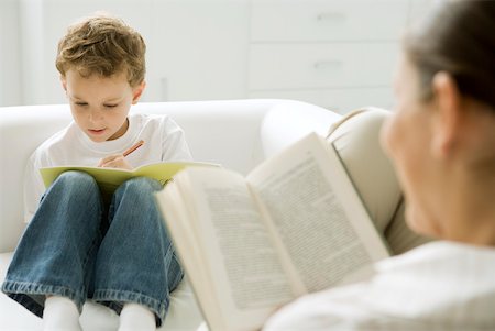 Boy sitting on sofa, writing in book, mother reading in foreground Stock Photo - Premium Royalty-Free, Code: 632-02282583