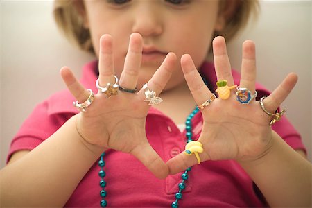 simsearch:632-02645173,k - Little girl wearing several plastic rings on fingers, close-up Fotografie stock - Premium Royalty-Free, Codice: 632-02645127