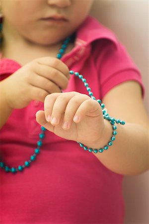 simsearch:632-02645173,k - Little girl wrapping beaded necklace around wrist, cropped Fotografie stock - Premium Royalty-Free, Codice: 632-02645177