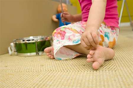 Little girl sitting on floor with toys, scratching foot, cropped view Foto de stock - Sin royalties Premium, Código: 632-02645173