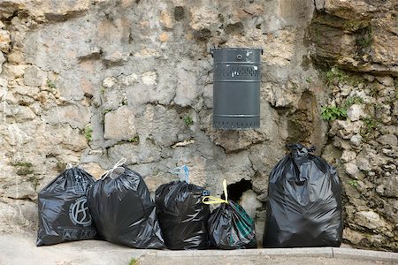 Several bags of garbage lined up along stone wall beneath mounted trash can Stock Photo - Premium Royalty-Free, Code: 632-02690420