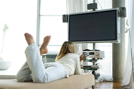 Female lying on stomach watching flat screen TV with surround sound, remote control in hand, rear view Stock Photo - Premium Royalty-Free, Code: 632-02744841