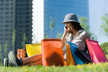 Young woman sitting on ground surrounded by shopping bags, talking on cell phone Stock Photo - Premium Royalty-Free, Code: 632-02745015