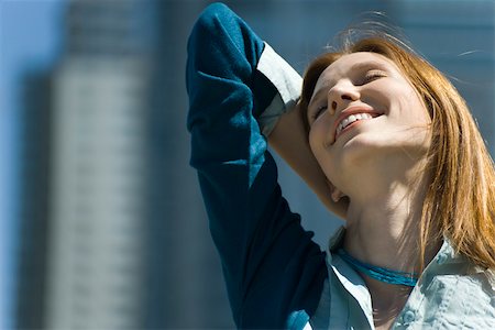 Young woman outdoors, smiling with one hand behind head and eyes closed Stock Photo - Premium Royalty-Free, Code: 632-02745024