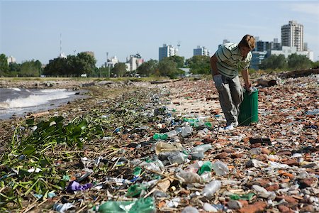 Person picking up trash on polluted shore, city in background Stock Photo - Premium Royalty-Free, Code: 632-02745053