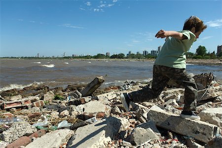 Boy running on shore littered with debris, city in background Foto de stock - Sin royalties Premium, Código: 632-02745094