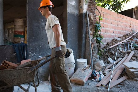 Construction worker moving wheelbarrow through construction site Stock Photo - Premium Royalty-Free, Code: 632-02885294