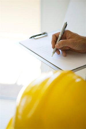 Hand writing notes on clipboard pad, hard hat in foreground, cropped view Stock Photo - Premium Royalty-Free, Code: 632-02885344