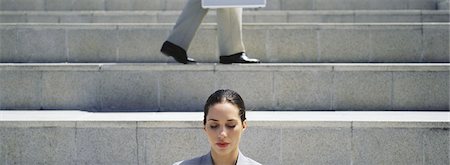 front and centre - Woman on steps with eyes shut, businessman walking in background Stock Photo - Premium Royalty-Free, Code: 632-03083029