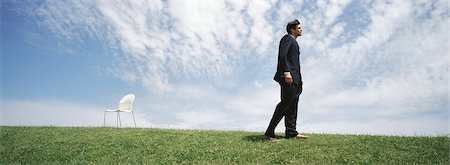 Businessman walking barefoot in grassy field, empty chair nearby Foto de stock - Sin royalties Premium, Código: 632-03083063