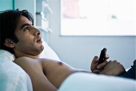 simsearch:632-01154764,k - Man reclining on bed holding cell phone, looking away contemplatively Foto de stock - Royalty Free Premium, Número: 632-03083188