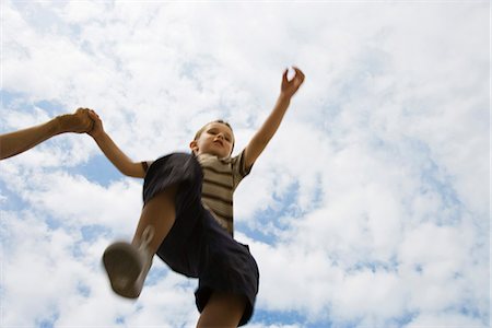 Boy holding adult's hand, jumping in midair, low angle view Stock Photo - Premium Royalty-Free, Code: 632-03083426