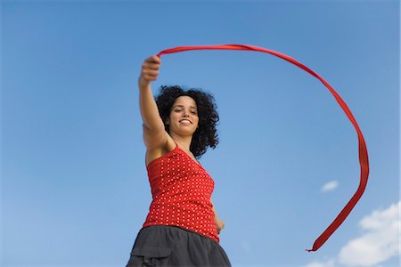 red ribbon - Young woman holding ribbon in wind, smiling, low angle view Stock Photo - Premium Royalty-Free, Code: 632-03083422