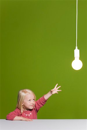 Little girl reaching for illuminated light bulb suspended overhead Stock Photo - Premium Royalty-Free, Code: 632-03193344