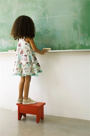 Little girl standing on stool in front of blackboard, rear view Stock Photo - Premium Royalty-Free, Code: 632-03193647