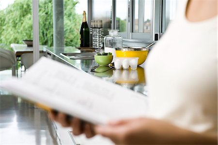 Reading recipe in cookbook, ingredients on kitchen counter in background Stock Photo - Premium Royalty-Free, Code: 632-03424298