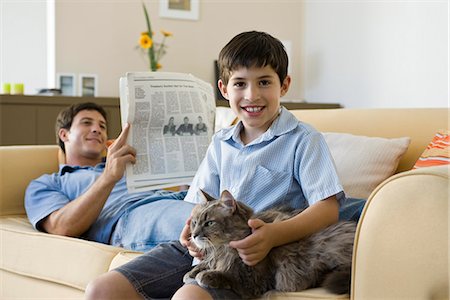 father and kids in lap - Young boy with pet cat on lap, father reading newspaper in background Stock Photo - Premium Royalty-Free, Code: 632-03424350