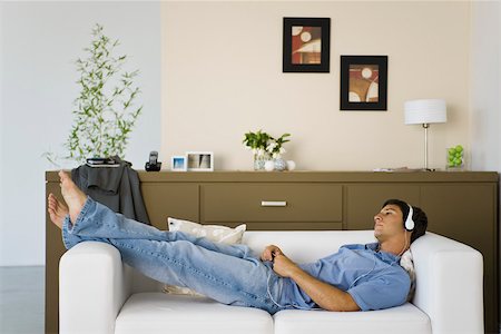 Young man relaxing on sofa listening to music with headphones Stock Photo - Premium Royalty-Free, Code: 632-03424361