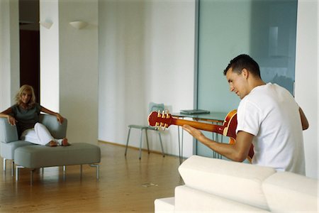 Man playing acoustic guitar in living room, woman watching Stock Photo - Premium Royalty-Free, Code: 632-03424730