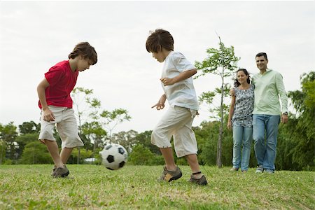 father kid run play - Boys playing soccer, parents watching in background Stock Photo - Premium Royalty-Free, Code: 632-03516975