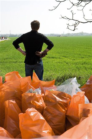 people cleaning rubbish - Man standing by pile of garbage bags after cleanup effort, rear view Stock Photo - Premium Royalty-Free, Code: 632-03651686