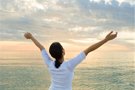 Woman watching sunset at the beach, arms raised in the air Stock Photo - Premium Royalty-Free, Code: 632-03651855