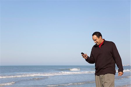L'homme cherche la messagerie texte sur téléphone cellulaire à la plage Photographie de stock - Premium Libres de Droits, Code: 632-03652034