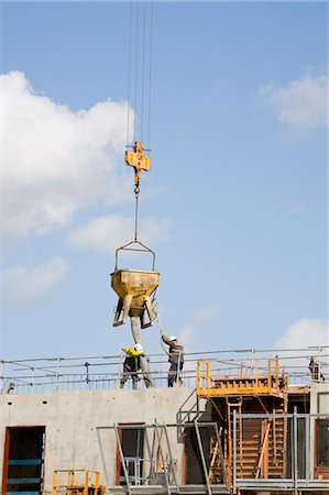 Construction workers guiding bucket suspended by crane to deposit concrete on building under construction Foto de stock - Sin royalties Premium, Código: 632-03652208