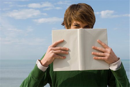 Young male holding book in front of face, portrait Stock Photo - Premium Royalty-Free, Code: 632-03652282