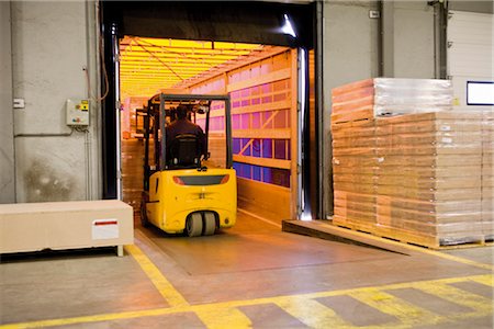 Forklift operator loading wrapped pallets of cardboard boxes onto trailer in warehouse Foto de stock - Sin royalties Premium, Código: 632-03754576