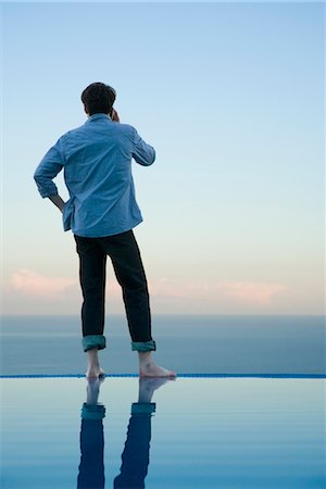 swimming pool phone - Man standing on edge of infinity pool, talking on cell phone Stock Photo - Premium Royalty-Free, Code: 632-03779609