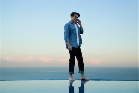 piscina desbordante - Man standing on edge of infinity pool, talking on cell phone Foto de stock - Sin royalties Premium, Código: 632-03779629