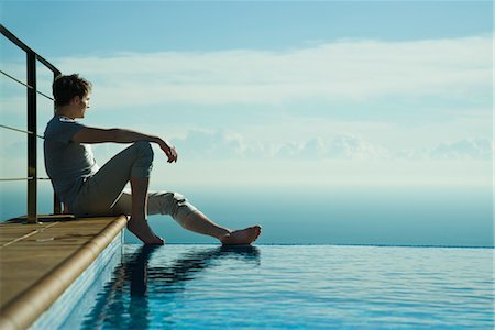 swimming pool edge - Man sitting on edge of infinity pool, looking at view Foto de stock - Sin royalties Premium, Código: 632-03779622