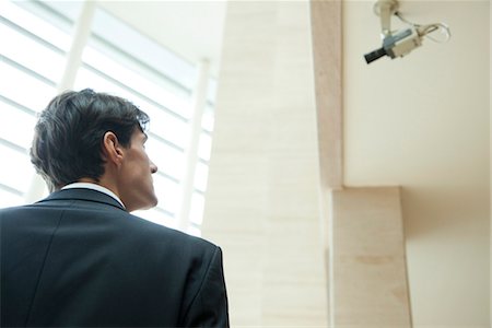 Businessman looking up at security camera Fotografie stock - Premium Royalty-Free, Codice: 632-03848097