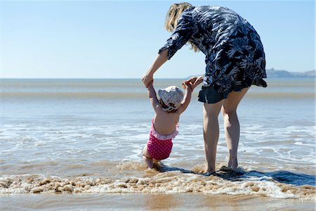 rear view of two children holding hands - Mother and baby daughter walking in surf at the beach, rear view Stock Photo - Premium Royalty-Free, Code: 632-03898006