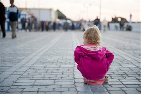 Toddler girl sitting on the ground in city square, watching people walk by Stock Photo - Premium Royalty-Free, Code: 632-03898169