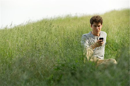 simsearch:400-08997106,k - Young man sitting in grass text messaging Stock Photo - Premium Royalty-Free, Code: 633-05401460