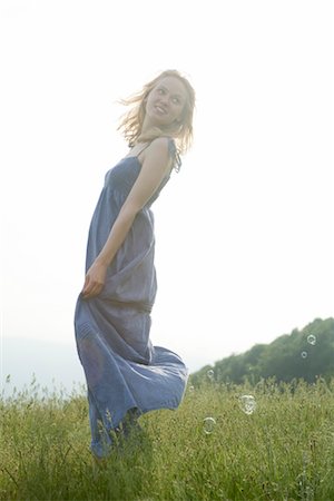 Young woman standing in meadow on breezy day, bubbles floating around her Stock Photo - Premium Royalty-Free, Code: 633-05401537