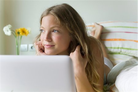 Young woman relaxing in bed with laZSop computer, looking away dreamily Stock Photo - Premium Royalty-Free, Code: 633-05401608