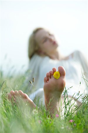 soles of feet - Pieds nus jeune femme assise dans l'herbe, tenant la fleur de pissenlit entre les orteils Photographie de stock - Premium Libres de Droits, Code: 633-05401823