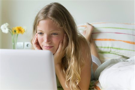 Young woman lying on stomach in bed, looking at laZSop computer Stock Photo - Premium Royalty-Free, Code: 633-05401877