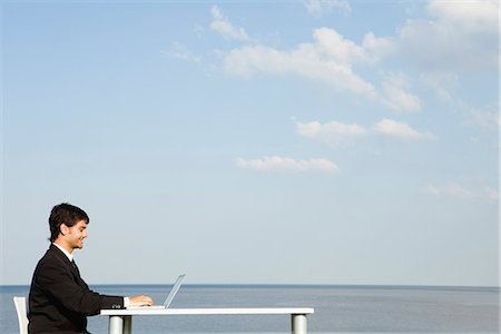 Young businessman working at desk by ocean, side view Stock Photo - Premium Royalty-Free, Code: 633-06322423