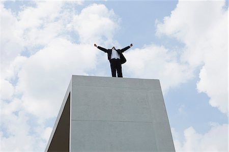Businessman standing on concrete structure with arms outstretched, low angle view Stock Photo - Premium Royalty-Free, Code: 633-06322623