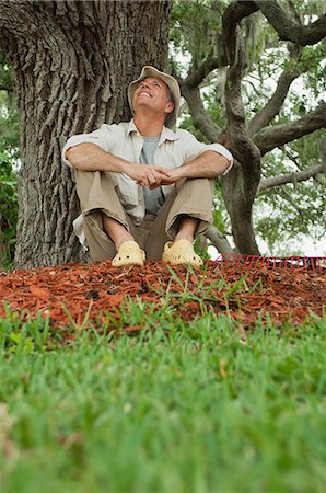 Mature man sitting under tree, looking up and smiling Stock Photo - Premium Royalty-Free, Code: 633-06354785